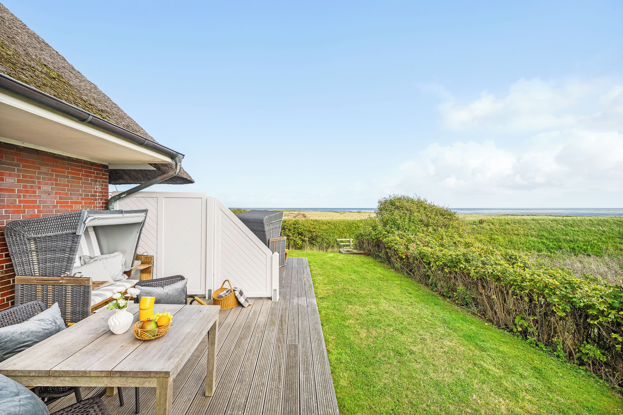 Eine Terrasse mit Esstisch, einem Korbstuhl und einem weißen Sofa.