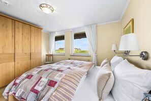 Un dormitorio con una cama grande, un armario de madera, dos ventanas con cortinas y vistas al exterior.