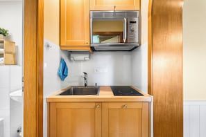 Une cuisine compacte dotée de meubles en bois, d’un évier en acier inoxydable, d’un four à micro-ondes encastré et d’une plaque de cuisson à induction.