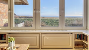 A room with a large window overlooking a coastal landscape, a brick wall, and a bookshelf. - Apartment Watt directly on the mudflats in Rantum on Sylt (Sylt)