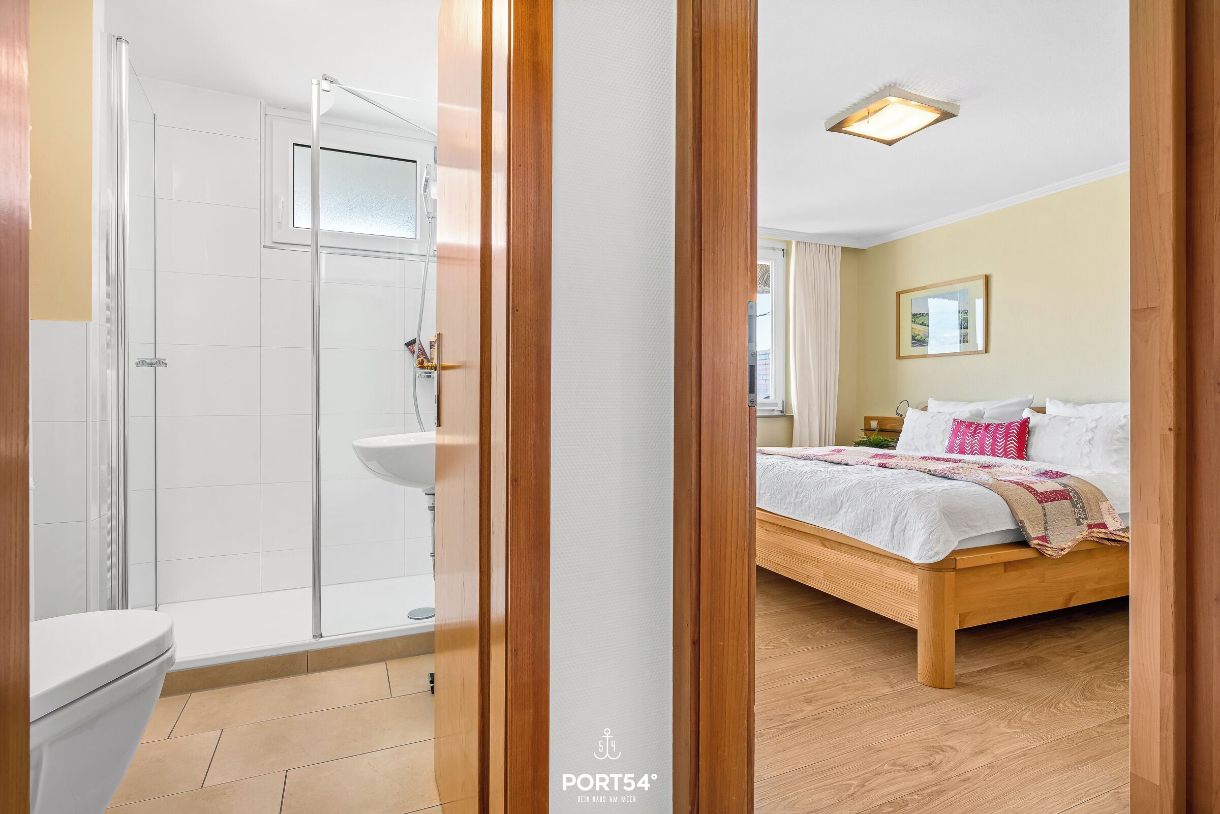 Ein Hotelzimmer mit einem hölzernen Bett, einem weißen Badezimmer mit Duschkabine und Blick ins Freie.