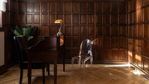Een hoekkamer met houten paneelwanden, een piano, een transparante plastic stoel en een lamp.