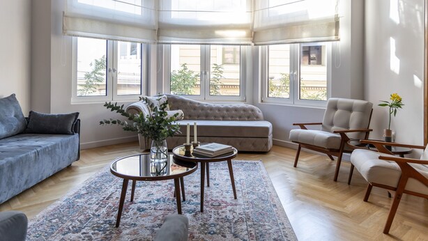 Een ruime woonkamer met een groot raam, een bank, een salontafel en een fauteuil.
