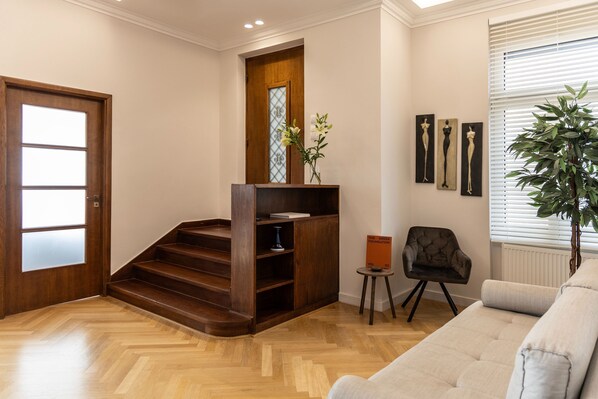 Un interno moderno con una scala in legno, un divano, un tavolino con un vaso e opere d'arte alle pareti.