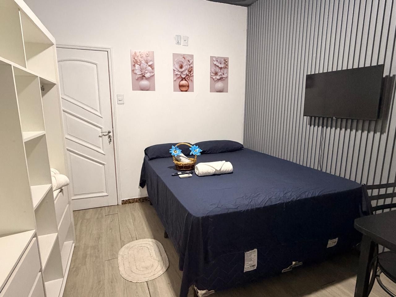 Un dormitorio con una cama, un armario, un televisor y tres cuadros colgados en la pared.
