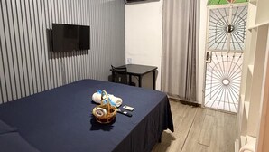 A hotel room with a bed, a TV mounted on the wall, a small table, and a door with a decorative glass panel.