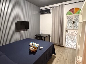 A hotel room with a bed, a TV mounted on the wall, a small table, and a door with a decorative glass panel.