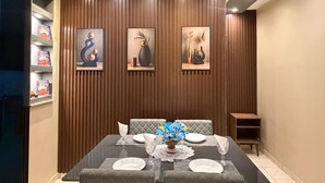 A dining area with a table set for four, a vase of flowers, and three framed artworks on the wall.