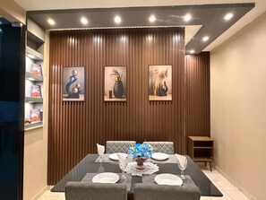 A dining area with a table set for four, a vase of flowers, and three framed artworks on the wall.