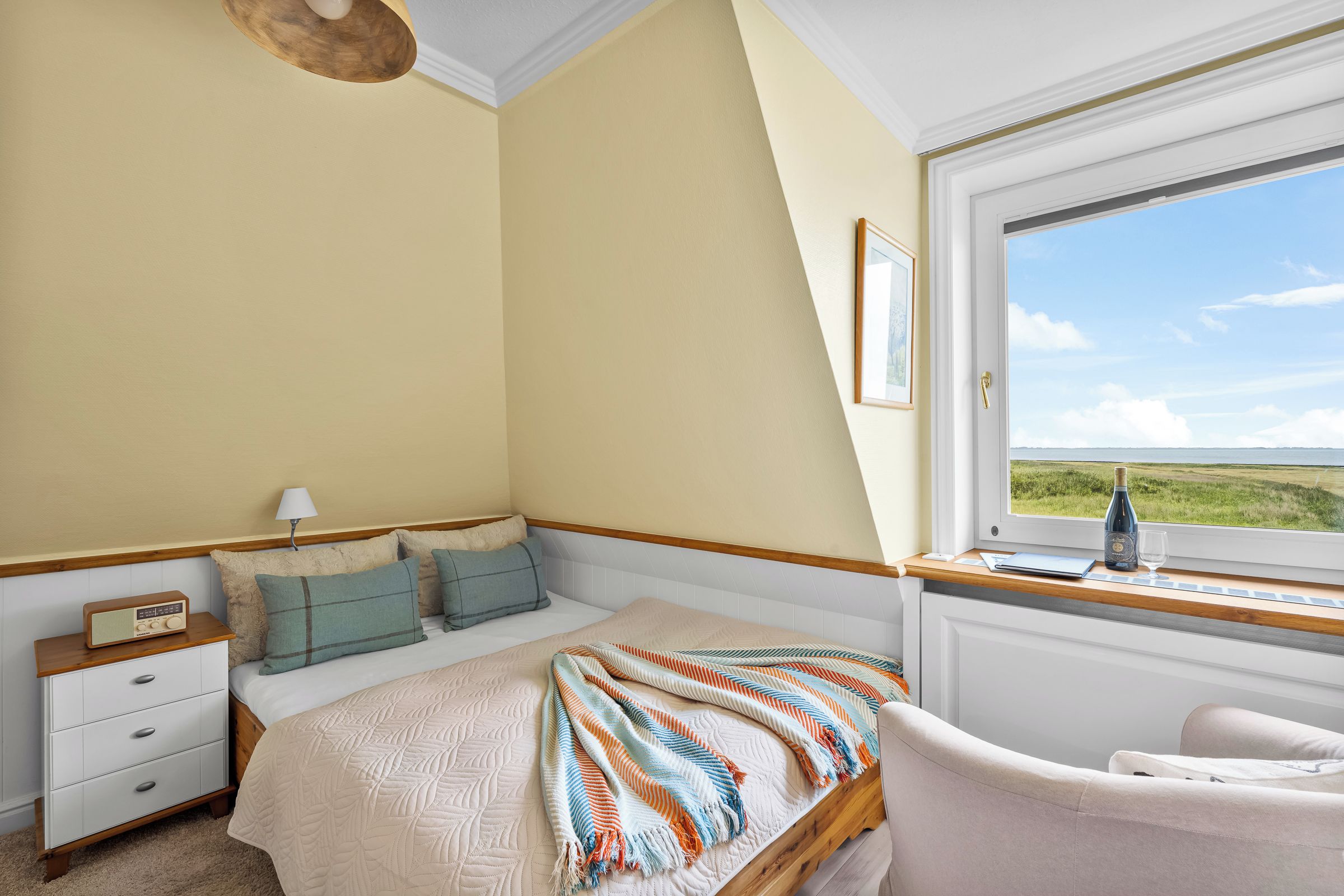 Een slaapkamer met een bed, nachtkastje, lamp en een raam met uitzicht op de omgeving.