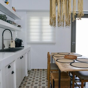 A modern kitchen with white cabinets, a black sink, and a wooden dining table with woven chairs. - Dream on  Adamas Milos (Adamas)