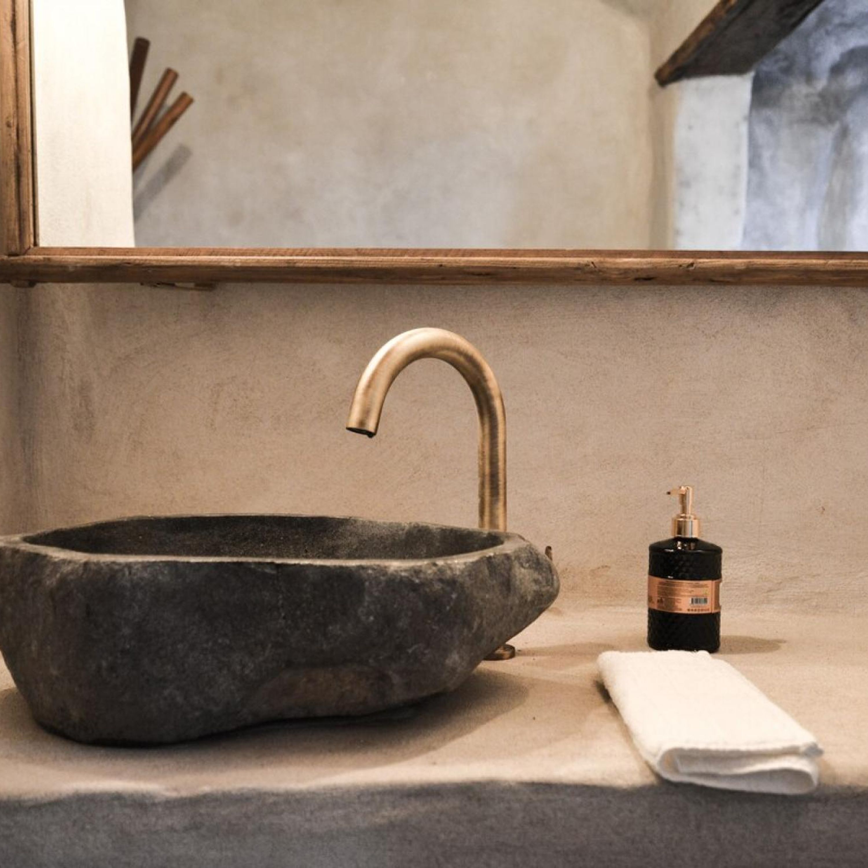 Un lavabo de piedra con un grifo curvo y una pequeña botella de jabón sobre una encimera.