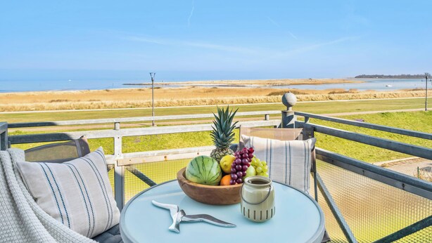 A balcony with a view of a beach, a table with a bowl of fruit, a cup, and a bird-shaped ornament. - Modern beachfront apartment in Stein with exceptional sea view and terrace (Stein)