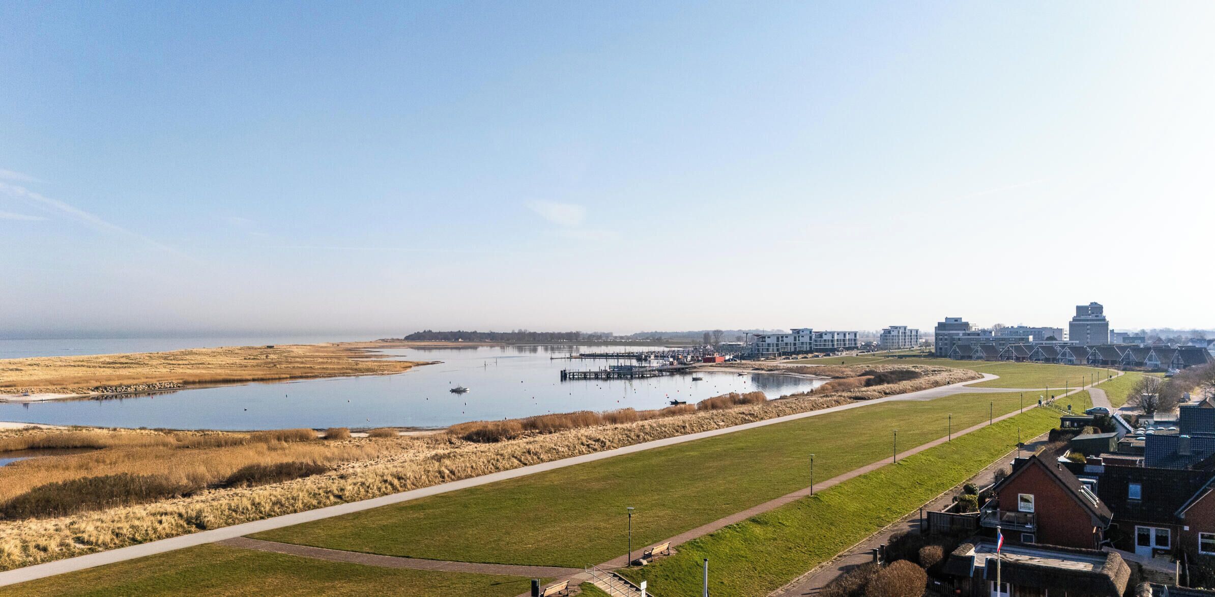 A coastal landscape with a large body of water, a walking path, and residential buildings in the background.