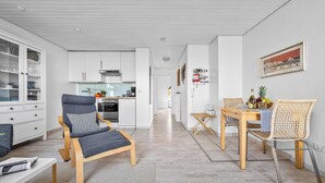 A modern kitchen with white cabinets, a dining area with a wooden table and wicker chairs, and a living area with a grey sofa. - Modern beachfront apartment in Stein with exceptional sea view and terrace (Stein)