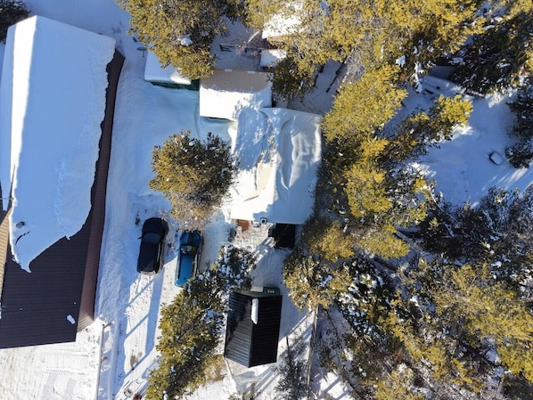 Vista aérea de un área residencial con suelo cubierto de nieve, un camino de entrada y una casa con garaje visible.