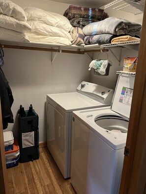 Een wasserette met een wasmachine, droger en bovenop planken voor opslag.