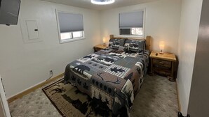 Une chambre à coucher avec un lit, deux tables de chevet, un luminaire au plafond, une fenêtre et une porte.