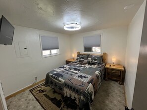 Een slaapkamer met een bed, twee nachtkastjes, een plafondlamp, een raam en een deur.