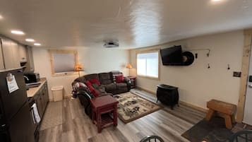 A compact living space with a kitchenette, a sofa set, a dining table, and a television mounted on the wall.