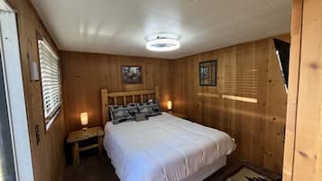 A wooden-paneled bedroom with a bed, bedside lamps, and a ceiling light fixture.