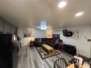 Een kleine woonruimte met een kitchenette, een zithoek, een salontafel en een flatscreen televisie aan de muur.