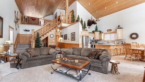 A spacious living room with a high ceiling, a staircase, a kitchen, and a dining area. - Paradise in the Pines | Hot Tub | 35 miles to YNP (Island Park)