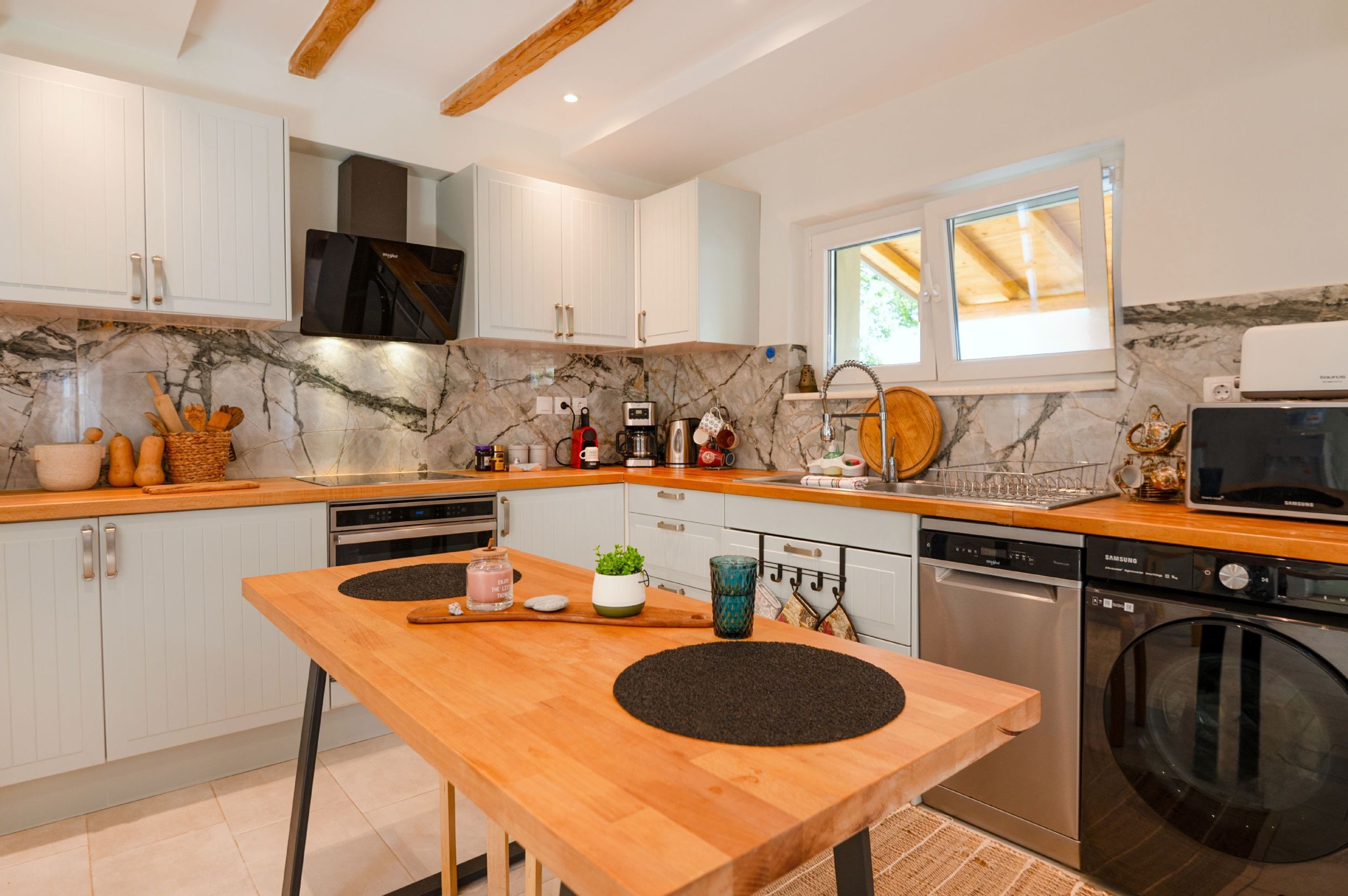 Una cocina moderna con armarios blancos, salpicadero de mármol y electrodomésticos de acero inoxidable.