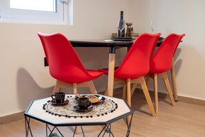Uma sala de jantar com uma mesa e quatro cadeiras vermelhas. Há uma chávena de café e um pastel na mesa.