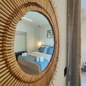Ein Zimmer mit einem großen, runden Spiegel mit Bambusrahmen, einem Bett mit blauer Bettwäsche und einer Wandleuchte.