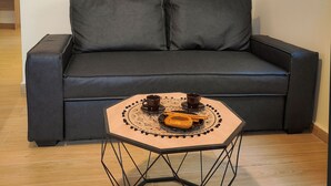 Un sofá gris oscuro con dos cojines, una mesa hexagonal con una bandeja decorativa y un mapa antiguo del mundo en la pared.