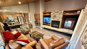 A modern living room with leather sofas, a coffee table, a fireplace, and a kitchen in the background. - Cozyville Cabin: Quiet Getaway, Built 2019 (Big Bear)