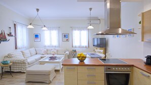 Een moderne keuken met een ingebouwde oven, een eethoek met een tafel en stoelen, en een woonkamer met een bank en een televisie.