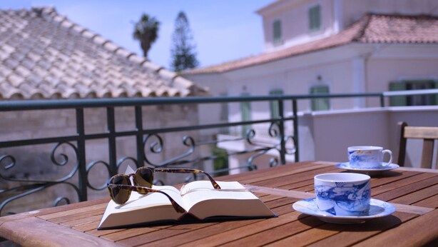 Een houten tafel met een open boek, zonnebril en een kopje op een balkon.