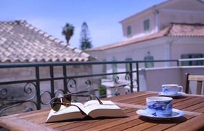 Una mesa de madera con un libro abierto, gafas de sol y una taza en un balcón.