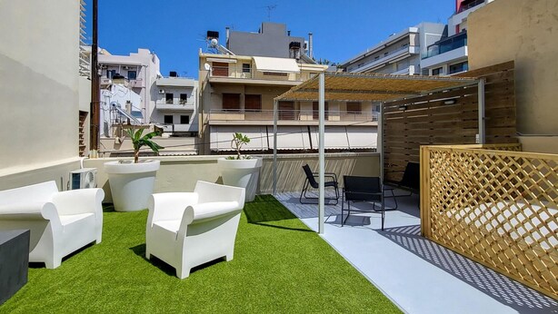 Eine Dachterrasse mit künstlichem Rasen, weißen Möbeln für draußen und einem Holzzaun.