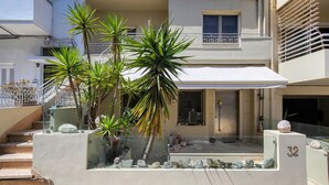 Ein mehrgeschossiges Wohngebäude mit Balkon, Treppe und einem kleinen Gartenbereich mit Pflanzen und dekorativen Steinen.