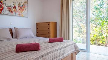 Un dormitorio con cama, cómoda de madera y ventana grande con vista a follaje.