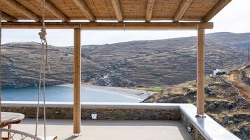 En overdækket terrasse med udsigt over et kystlandskab, inklusive en strand og bakker.