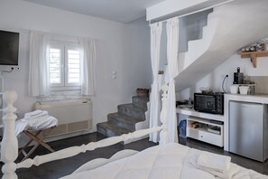 Une chambre avec un lit, une petite table et une chaise, une fenêtre avec des rideaux, un escalier et une kitchenette équipée d’un four à micro-ondes et d’un réfrigérateur.