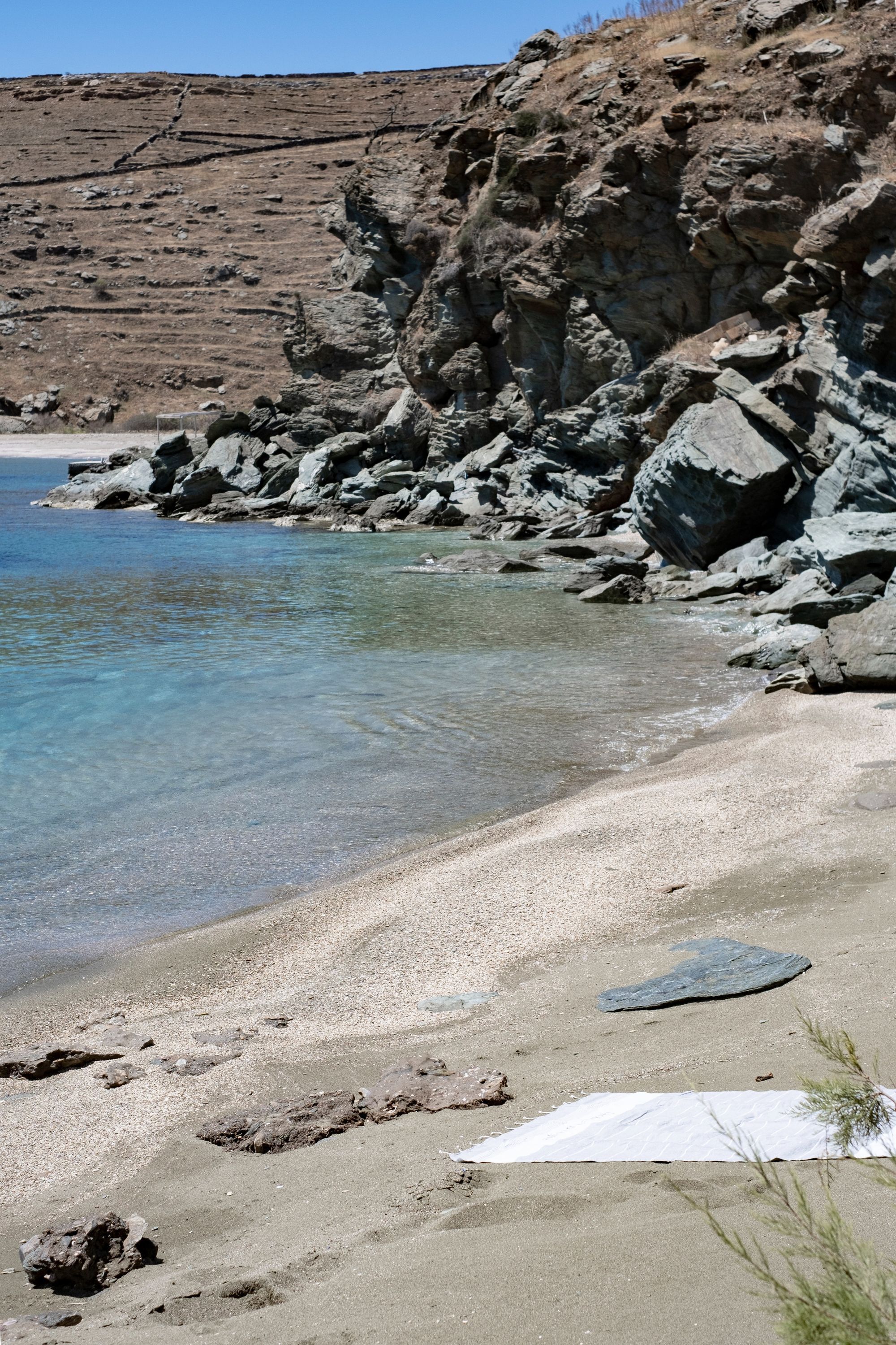 A rocky beach with clear water, pebbles, and a white object on the sand.