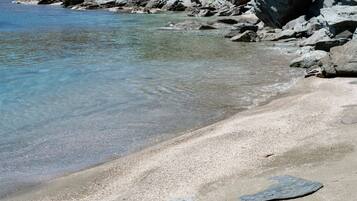 A rocky beach with clear water, pebbles, and a white object on the sand.