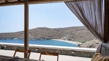 A wooden table and chairs under a pergola with a view of a beach and hills.