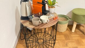 Une petite table ronde avec une machine à café, des tasses, une plante et un pouf vert.