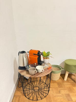 Ein kleiner runder Tisch mit einer Kaffeemaschine, Tassen, einer Pflanze und einem grünen Hocker.