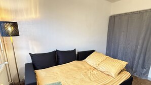 Une chambre à coucher avec un lit, une lampe sur pied, une fenêtre avec des rideaux et un tapis à motifs.