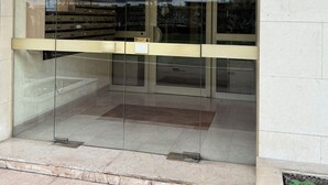 Une entrée d’immeuble avec des portes vitrées, une plaque signalétique et un numéro d’immeuble.