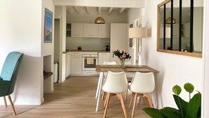 A modern kitchen with white cabinets, a wooden dining table with chairs, and a hanging light fixture. - Cosy, quiet house close to the oyster port. (La Teste-de-Buch)