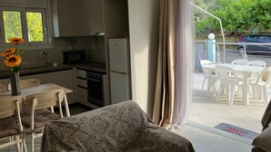 Una cucina compatta con lavello, fornelli e frigorifero, una zona pranzo con tavolo e sedie, e vista su un paesaggio verde attraverso un'ampia finestra.