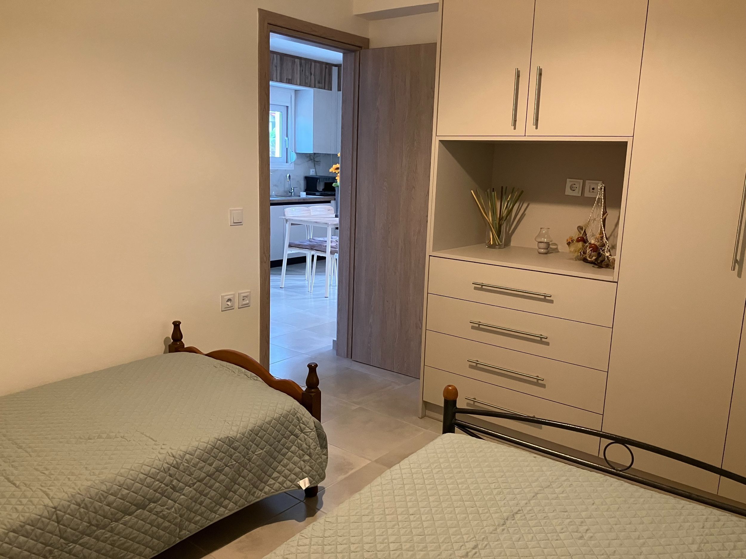 A bedroom with two beds, a wardrobe, and a view into the kitchen.